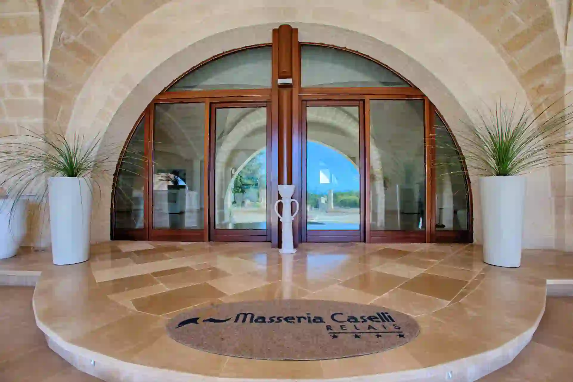 Entrance to Masseria Caselli Hotel, Italy, featuring arched stone architecture, large glass doors, and modern planters